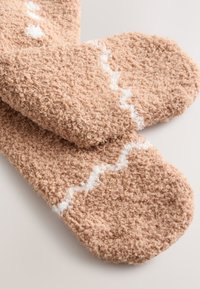 Bruine pluizige sokken met een getextureerd oppervlak en een wit zigzagpatroon. De vorm is afgerond bij de tenen en overal zacht en pluizig.