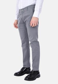 Pantaloni grigi realizzati in un tessuto liscio, caratterizzati da un design aderente e una chiusura con un solo bottone, abbinati a eleganti scarpe nere lucide.