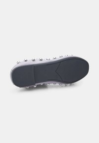 Suela de zapato con una base de goma negra texturizada, tachuelas metálicas a lo largo del borde y una parte superior de color gris claro. Presenta un logotipo estampado en la suela.