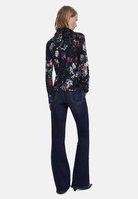Top a maniche lunghe floreale con sfondo nero e fiori colorati; abbinato a jeans svasati scuri, che mettono in risalto silhouette casual e aderenti.