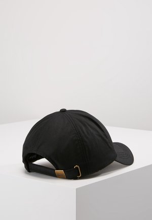 Zwarte verstelbare honkbalpet met metalen gesp sluiting, rustend op een wit oppervlak met hoeken, tegen een effen lichte achtergrond.