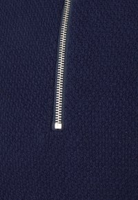 Navy gestrickter Pullover mit einem halben Reißverschluss und einem silbernen Metall-Reißverschluss. Die Textur hat eine subtile Musterung.