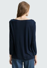 Mörkblå långärmad topp med vid halsringning, mjukt draperat tyg och avslappnad passform. Har uppvikta ärmslut och en böjd nederkant.