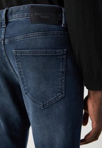 Granatowe dżinsy z tylnymi kieszeniami, haftowanymi detalami i czarną skórzaną metką w pasie z napisem "Marc O'Polo DENIM."