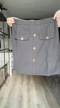 Gonna grigia con tasche frontali, pattina con bottoni argentati e struttura liscia. Design a metà lunghezza e strutturato.