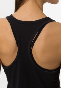 Top negro sin mangas con diseño de espalda nadadora, que cuenta con tirantes ajustables y una textura de tela suave y lisa. La vista trasera resalta el ajuste al cuerpo.