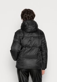 Zwarte pufferjack met een capuchon, geplooide secties, glanzende textuur en elastische manchet. Op de rug bevindt zich een logo op de linkerschouder.