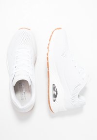 Weiße Sport-Sneaker mit perforiertem Obermaterial, Schnürdesign und einer gepolsterten Sohle mit einer klaren Luftblase. Orangene Gummisohlen-Details.
