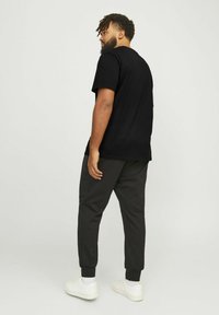 Schwarzes kurzärmliges T-Shirt in lässiger Passform, kombiniert mit dunkelgrauen Jogginghosen mit elastischen Bündchen, getragen mit weißen Sneakern.