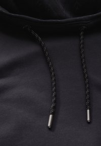 Sudadera negra con una capa exterior texturizada, que presenta cordones negros con puntas metálicas y un material interior suave.