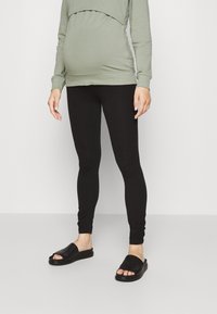 Leggings noires associées à un sweat-shirt vert, avec une coupe décontractée, un tissu doux et un design longueur cheville. Porté avec des sandales noires.