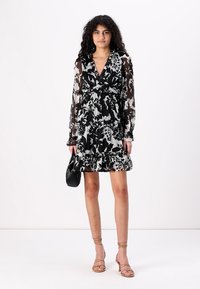 Haljina s cvjetnim printom u crno-bijeloj boji, dugim prozirnim rukavima, volanima na rubu i dizajnom omota. Uparena s malom crnom torbicom i sandalama s trakama.