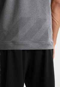 T-shirt de sport gris avec un motif texturé ; comprend des accents en mesh respirant et une finition en tissu lisse aux ourlets et aux manches.