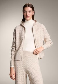 Béžový kardigan s kapucí s vzorem copánkového pletení, zapínáním na zip a žebrovanými manžetami, doplněný o kalhoty ve stejném designu.