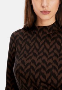 Braun gemustertes Kleid mit hohem Ausschnitt, das ein Zickzackmuster in Dunkelbraun auf einem hellbraunen Hintergrund zeigt, glatte Textur.