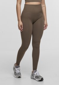 Brown high-waisted leggings made of stretchy material, featuring a smooth texture and a fitted design, worn with gray athletic shoes.