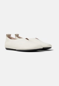 Zapatos slip-on de cuero blanco con un diseño minimalista, puntera redondeada, suela plana de goma negra y pequeñas pestañas de tela en el talón.