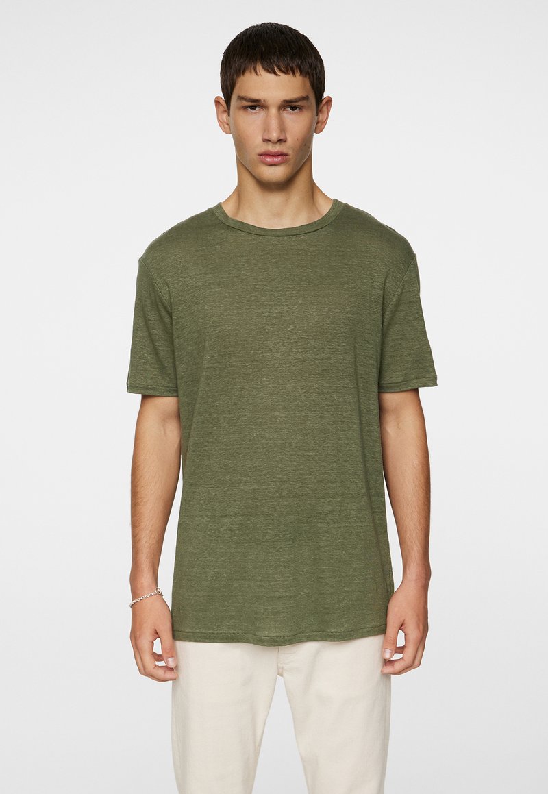 T-shirt vert olive à manches courtes avec un col rond, coupe décontractée, en tissu texturé, accompagné d'un pantalon de couleur claire.