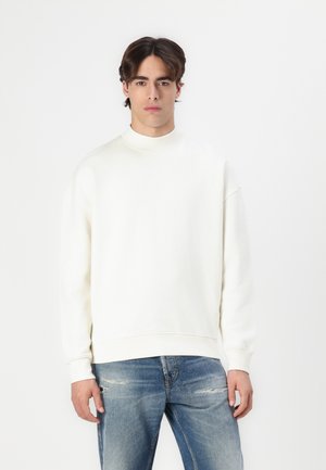 Hvit sweatshirt med høy hals, ribbestrikkede ermer og kant. Kombinert med lyseblå slitte jeans, som viser en avslappet passform og minimalistisk design.