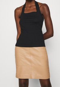 Svart ribbad halterneck-topp med fyrkantig uringning, kombinerad med en åtsittande beige läderminikjol med mittsydd söm. Slät struktur överlag.