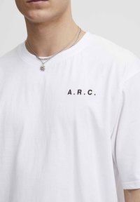 Hvid bomulds t-shirt med rund hals, korte ærmer og bogstaverne "A.R.C." trykt i sort på venstre brystområde.