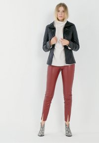 Schwarze Lederjacke mit Reißverschlüssen, cremefarbener Rollkragenpullover, bordeauxrote Lederhosen mit Schlitzen und graue Stiefeletten im Schlangenmuster.
