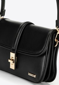 Bolso de mano de cuero negro con un diseño estructurado, herrajes dorados, cierre de clasp en la parte delantera y el nombre de la marca "WITTCHEN" exhibido de manera prominente.