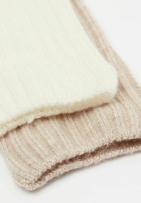 Dwa kawałki dzianiny, jeden w kolorze kremowym i puszystym, a drugi jasnobeżowy z ryżowym wzorem. Oba prezentują miękkie, przytulne materiały.