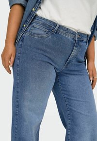 Vaqueros de mezclilla azul claro con corte recto, que cuentan con bolsillos delanteros y cremallera. Textura suave con sutiles detalles de desgaste.