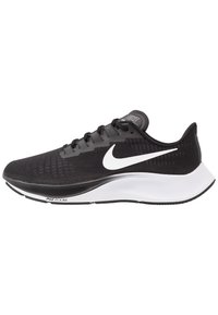 Chaussure de sport noire avec une tige en maille respirante, un swoosh Nike blanc et une semelle intermédiaire blanche rembourrée. Présente un tissu texturé et une semelle extérieure en caoutchouc.