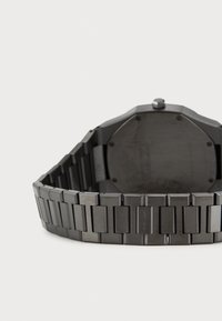 Montre noir avec un boîtier octogonal et un bracelet à maillons, présentant une texture lisse et des accents polis, vue de l'arrière.