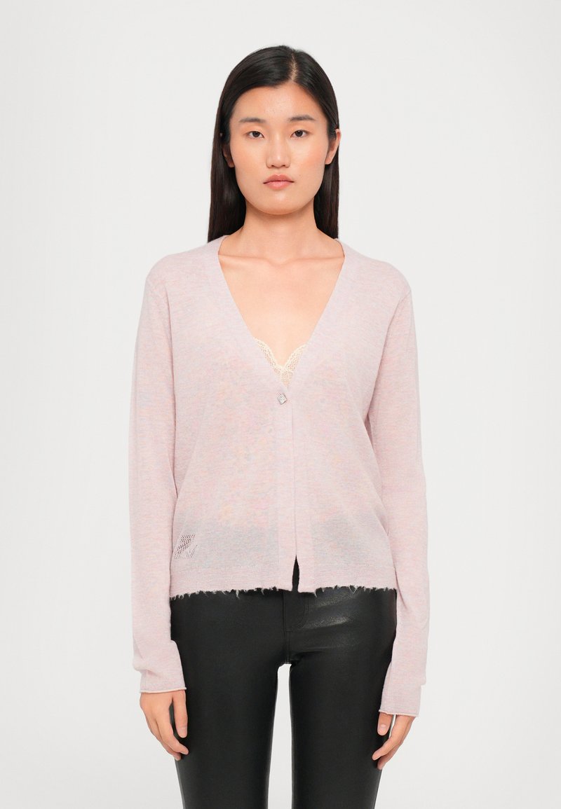 Helle rosa Strickjacke mit tiefem V-Ausschnitt, einem einzelnen Knopfverschluss, ausgefranstem Saum und gerippten Bündchen, die über einem Spitzentop getragen wird.