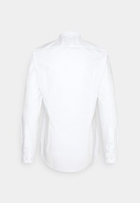 Chemise blanche à manches longues avec poignets boutonnés, vue de dos sur un fond clair uni.