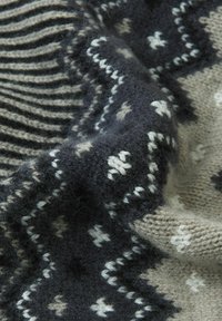 Vlněná tkanina s vzorem ševron v tmavě šedé a béžové barvě, s bílými akcenty v geometrických designech a texturovaným hřebenovým vzorem.
