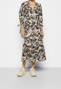 Kukallinen kietaisumekko, jossa on V-kaula-aukko, kolmanneksipitkät puffihihat ja kerroksellinen helma vaaleancremessä, mustassa ja beigeissä sävyissä. Valkoiset paksupohjaiset tunikakengät käytössä.