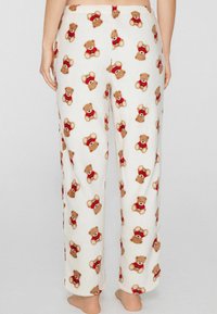 Fleecové pyžamové kalhoty s celoplošným potiskem kreslených medvídků v červených svetrech na krémovém pozadí; volný střih s elastickým pasem.