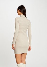 Abito a coste beige con maniche lunghe e collo alto, caratterizzato da strisce orizzontali nella parte superiore e una silhouette aderente.