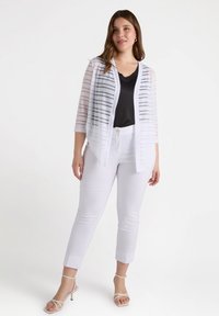 Witte gestreepte cardigan met open voorkant, gemaakt van lichte stof. Gemaakt over een zwarte top en gecombineerd met witte cropped pants en beige sandalen met banden.
