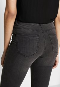 Jeans de mezclilla gris oscuro con un diseño ajustado, que cuentan con dos bolsillos traseros y una textura suave. La cinturilla está ubicada en la cintura natural.