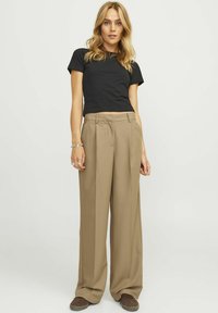 Un t-shirt noir ajusté associé à un pantalon beige taille haute, présentant un design à jambe large et une texture douce. Des baskets brunes complètent le look.