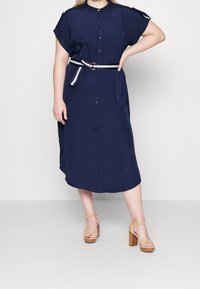 Námořnická modrá košilová šaty s krátkým rukávem a páskem s zlatou sponou. Hladká textura s uvolněným střihem. Boty na podpatku.