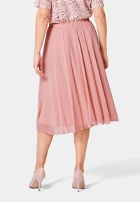 Roze geplisseerde rok van lichtgewicht stof, met een elastische tailleband en een vloeiende uitstraling, gecombineerd met lichtgekleurde hoge hakken.