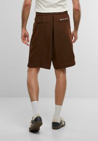 Braune Shorts mit lockerer Passform, ausgestattet mit einer Gesäßtasche und bestickten Details. Glatte Textur, knielang und mit einem leichten Aufschlag am Saum.