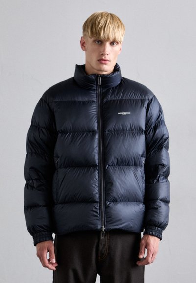 Navy puffer jacket made of shiny fabric, featuring a high collar, front zipper, and horizontal quilted pattern with elastic cuffs.