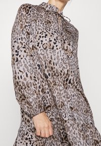 Šaty s leopardím vzorem v světlých béžových a hnědých tónech, s volánovým límcem, stahovací šňůrkou a vrstveným designem s balónovými rukávy.