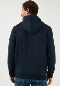 Felpa con cappuccio blu navy realizzata in tessuto morbido, dotata di tasca a marsupio e polsini rib elasticizzati sulle maniche e sull'orlo inferiore.