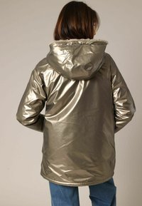 Parka argent métallique avec une capuche en fourrure, manches longues et coupe décontractée, présentant une texture brillante et un ourlet droit.