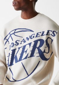 Pulover tricotat de culoare crem, cu inscripția "Los Angeles Lakers" în text de culoare albastră închisă și un grafic cu o minge de baschet. Guler rotund cu bordură, croială relaxată.