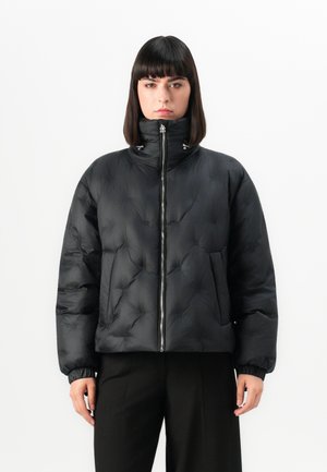 Veste matelassée noire avec un col haut, fermeture éclair et texture froncée. Dispose de poignets élastiques et de deux poches avant. Tissu lisse et brillant.