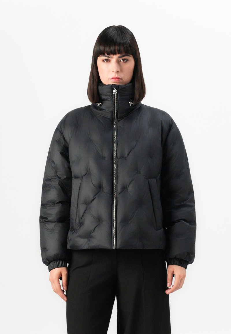 Giacca a vento nera con colletto alto, chiusura con zip e texture arricciata. Presenta polsini elastici e due tasche frontali. Tessuto liscio e lucido.